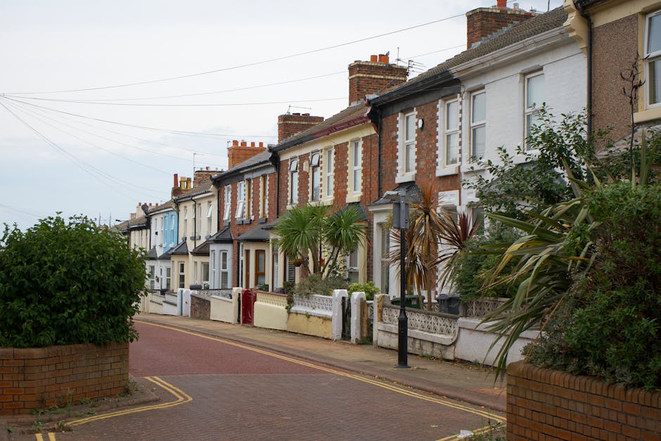 A whitebox van parked on a narrow, uphill residential street surrounded by multi-storey brick and stucco buildings. The van is positioned close to the curb outside a tall, multi-story building with la
